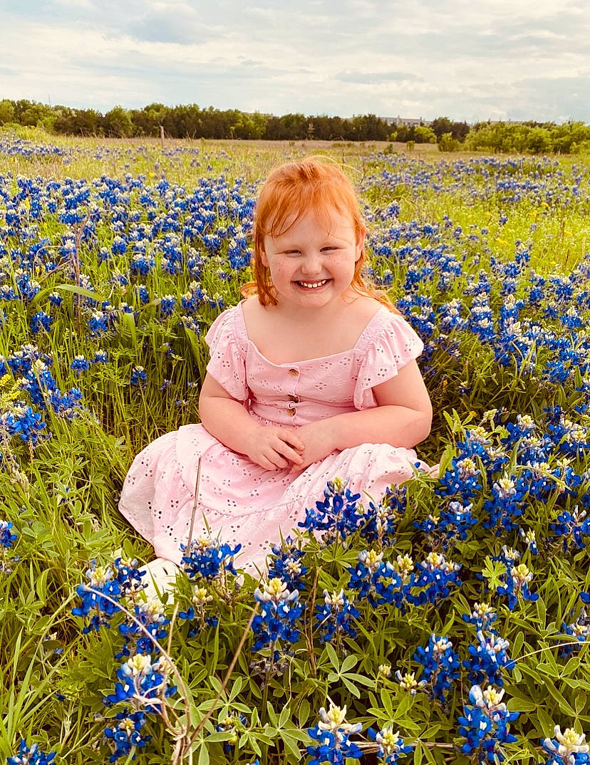 Ashlynn is registered to the contest to win money with this photo: baby_toddler_clothing, botany, cloud, flower, flowering_plant, grass, grass_family, grassland, groundcover, happy, joy, meadow, natural_environment, people_in_nature, person, petal, plant, prairie, sky, smile