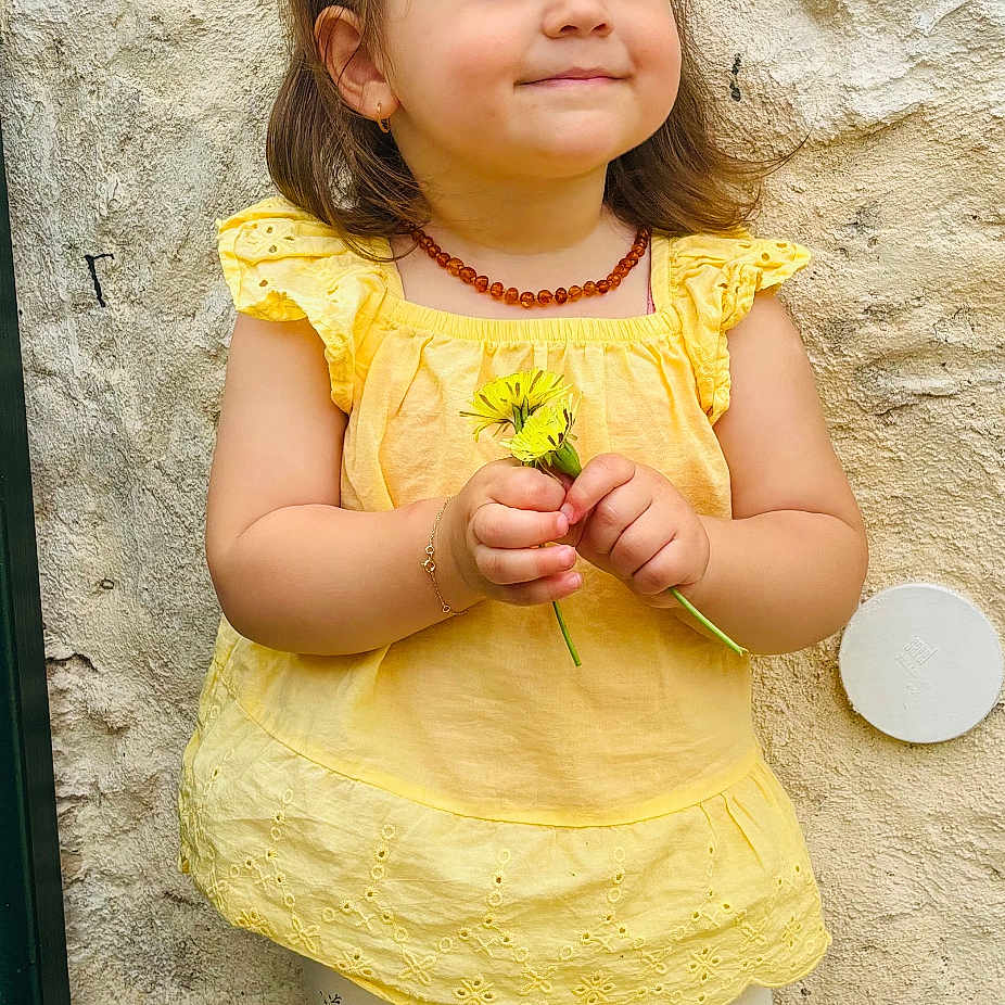 Alessia a rejoint le concours — aidez-le/la à gagner de superbes lots ! bracelet, child, cute, earrings, feet, flowers, hair_tie, happy, leggings, necklace, outdoor, pony_tail, portrait, shoes, smile, standing, texture, toddler, wall, yellow_top