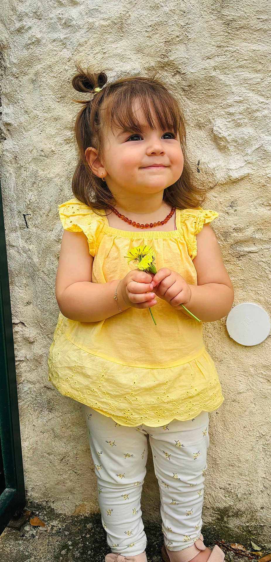 Alessia a rejoint le concours — aidez-le/la à gagner de superbes lots ! toddler, child, yellow_top, leggings, flowers, smile, standing, bracelet, necklace, hair_tie, pony_tail, wall, outdoor, cute, happy, portrait, feet, shoes, earrings, texture