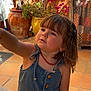 Alessia participe au concours pour gagner de l'argent avec cette photo : toddler, child, denim_dress, curly_hair, indoor, potted_plants, flowering_plant, orange_wall, sunlight, earrings, necklace, tiles, reaching_hand, cute, portrait, casual_clothing, brown_hair, curious_expression, decor, home