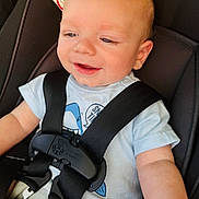 Eli is registered to the contest to win money with this photo: baby, car_seat, child, smiling, harness, seatbelt, infant, blue_shirt, light_hair, warning_label, safety, cute, portrait, closeup, happy, child_seat, person, straps, young_child, infancy