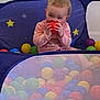Violet is registered to the contest to win money with this photo: baby, child, pink_onesie, ball, ball_pit, colorful, indoor, playtime, happy, smiling, face, head, sitting, toy, fun, stars, background, young_child, cute, playful