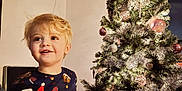 Greyson joined the competition — help win amazing prizes! child, toddler, christmas_tree, holiday, festive_clothing, pajamas, blond_hair, indoors, decorations, ornaments, lights, silver_tinsel, smiling, happy, young_child, celebration, seasonal, home, festivity, cute