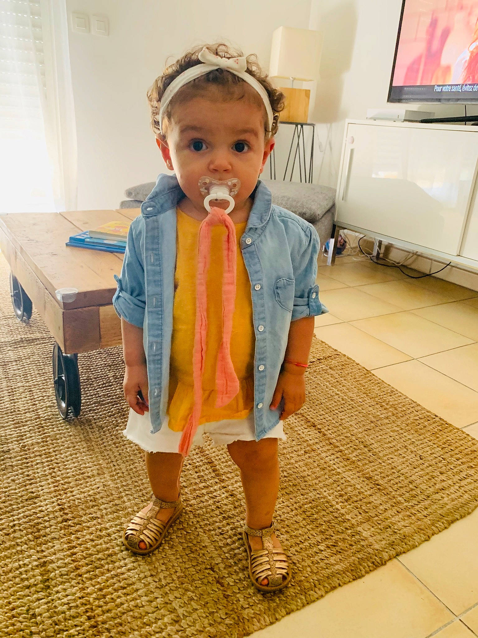 Mila participe au concours pour gagner de l'argent avec cette photo : baby_toddler_clothing, child, eye, fashion_accessory, floor, flooring, fun, happy, headband, home_appliance, person, room, shoe, shoulder, sleeve, smile, surprise, table, television, television_set