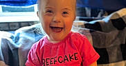 Jean Grey joined the competition — help win amazing prizes! blanket, bright_color, checkered_pattern, child, clothing, curtain, cute, expression, face, happy, indoor, joy, person, pink_shirt, portrait, seated, smiling, text_on_clothing, toddler, young_child