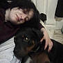 Fuzzy is registered to the contest to win money with this photo: person, dog, indoor, cuddle, affection, black_dog, hair, hand, floor, clothing, white_shirt, dark_hair, relaxation, pet, friendship, casual, blur, portrait, companion, home