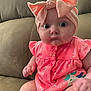 baby, infant, pink_bow, headband, onesie, unicorn_patch, couch, seated, wide_eyes, cute, child, indoors, portrait, clothing, soft_fabric, expression, hand, face, small_person, adorable