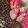 baby, infant, pink_bow, headband, pink_clothing, leopard_print, blanket, cute, cheeks, fingers, hand, lying_down, pattern, animal_print, smiling, indoors, child, portrait, cozy, soft