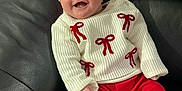Renesmé is registered to the contest to win money with this photo: baby, infant, smiling, red_bow, headband, white_sweater, red_pants, white_socks, leather_couch, black_couch, happy, cute, child, portrait, indoors, seated, clothing, fashion, cozy, young
