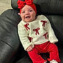 baby, infant, smiling, red_bow, headband, white_sweater, red_pants, white_socks, leather_couch, black_couch, happy, cute, child, portrait, indoors, seated, clothing, fashion, cozy, young