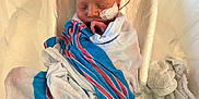 Benny is registered to the contest to win money with this photo: newborn, baby, hospital, blanket, bassinet, medical_tube, wrapped, sleeping, infant, plastic_bassinet, hospital_room, towel, patient, child, face, peaceful, healthcare, care, medical, resting