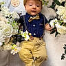 baby, infant, child, flower_arrangement, white_flowers, yellow_flowers, blanket, bow_tie, cap, suspenders, pants, cute, portrait, celebration, mother's_day, soft_texture, laying_down, happy, decorative, outdoor_style