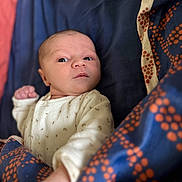 Mahiné a rejoint le concours — aidez-le/la à gagner de superbes lots ! baby, infant, blanket, blue, orange, pattern, onesie, clothing, face, skin, hand, lying_down, portrait, indoor, young_child, newborn, expression, cozy, soft_focus, curious