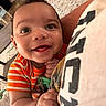 Kayden is registered to the contest to win money with this photo: baby, child, smiling, happy, indoor, striped_clothing, orange_clothing, holding, person, face, eyes, hand, floor, rug, pattern, shirt, text, closeup, cute, joy