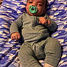 baby, infant, pacifier, blanket, pajamas, green_clothing, lying_down, cute, indoors, child, cozy, face, person, newborn, toddler, patterned_blanket, sleepwear, small_hands, expression, resting