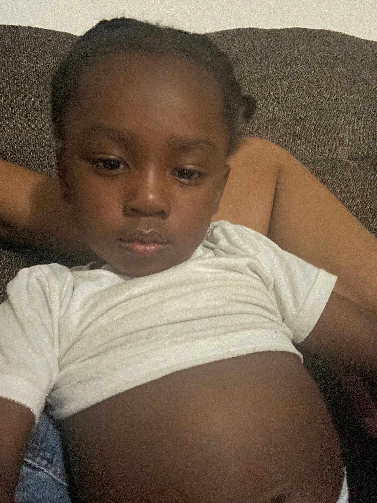 Tyaun is registered to the contest to win money with this photo: child, young_child, indoor, couch, white_shirt, relaxed, portrait, brown_background, person, casual, sitting, calm, closeup, face, expression, skin, hair, comfort, home, resting