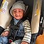 baby, baby_hand, car_seat, casual, child, clothing, comfortable, cute, denim_overalls, hat, headwear, indoor, infant, person, seatbelt, sitting, smiling, striped_shirt, wood_floor, young_child