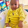 Zion joined the competition — help win amazing prizes! baby, child, smile, yellow_clothing, teddy_bear_pattern, chair, infant, cute, indoor, portrait, happy, sitting, person, young_child, cozy, soft_lighting, face, baby_bottle, furniture, closeup
