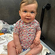 Adèle a rejoint le concours — aidez-le/la à gagner de superbes lots ! baby, child, onesie, floral_pattern, blue_eyes, smiling, sitting, changing_table, indoor, skin, hand, foot, hair, face, cute, infant, clothing, person, happy, room