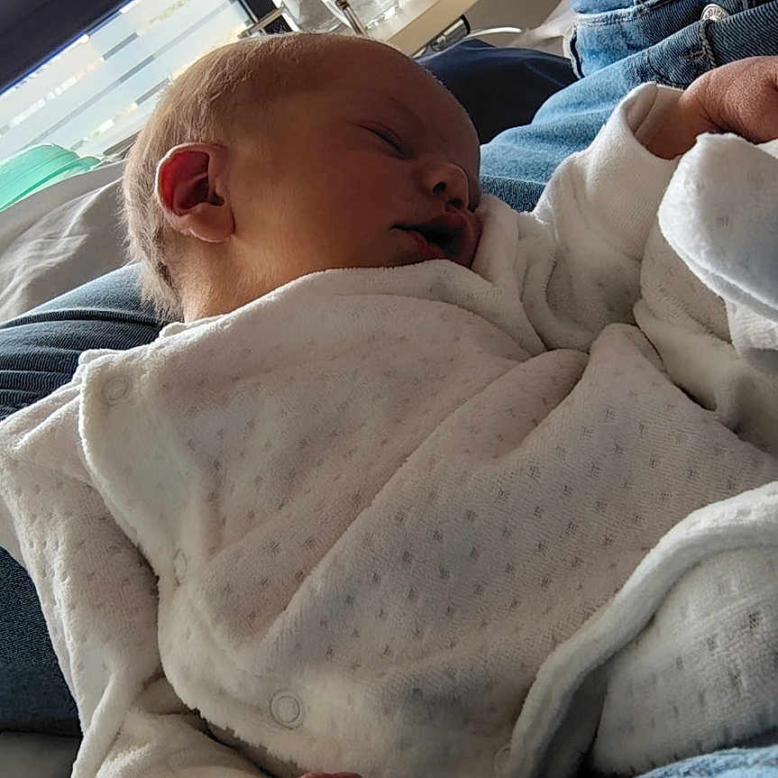 Eléonore a rejoint le concours — aidez-le/la à gagner de superbes lots ! baby, newborn, sleeping, infant, person, clothing, white_outfit, hand, lap, blue_jeans, window, daylight, glass_bottle, cup, tray, bed, blanket, indoor, peaceful, portrait