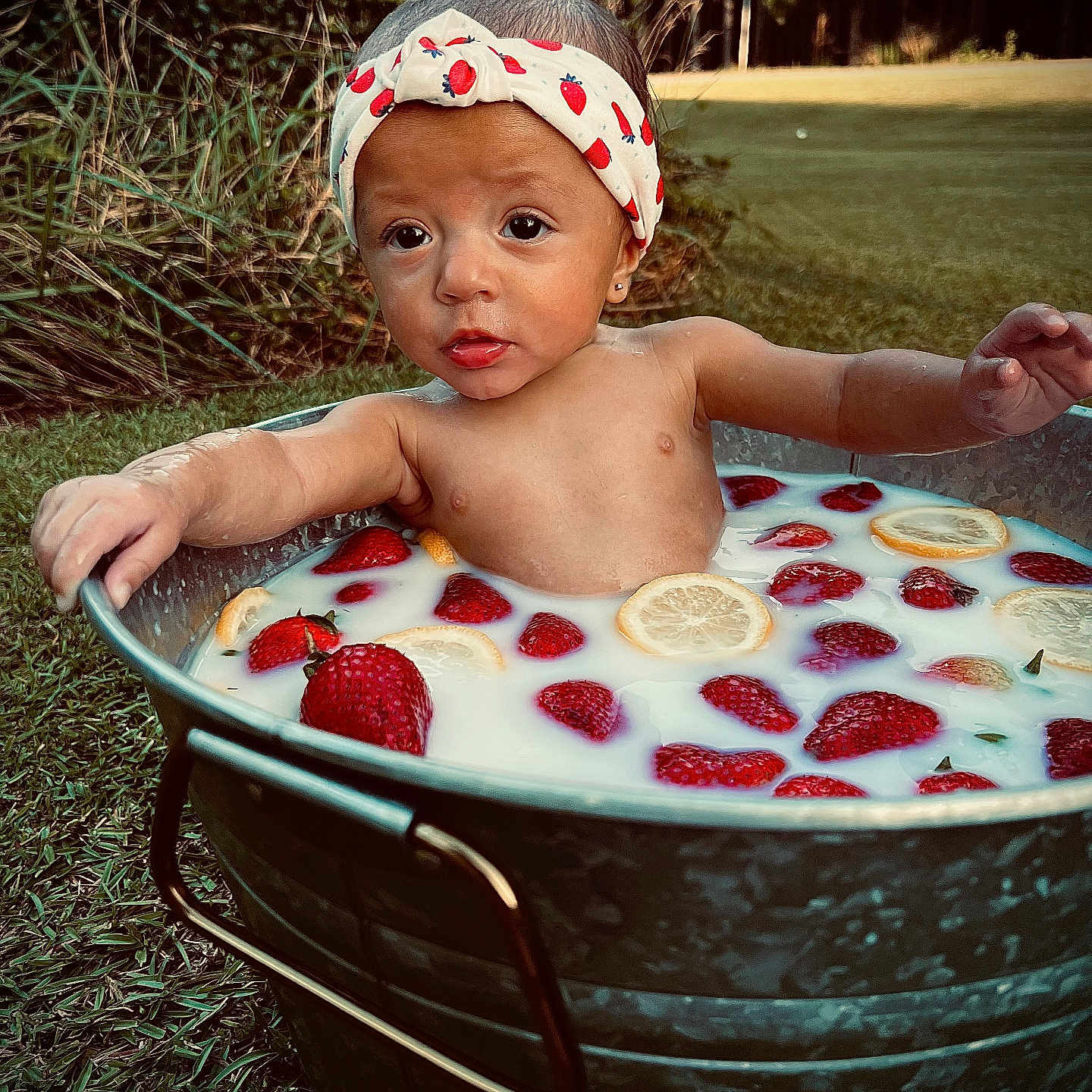 Lily is registered to the contest to win money with this photo: baby, child, cute, earrings, expression, fruit, grass, headband, lemon_slices, metal_tub, milk, nature, outdoor, plants, portrait, relaxing, skin, strawberries, summer, water