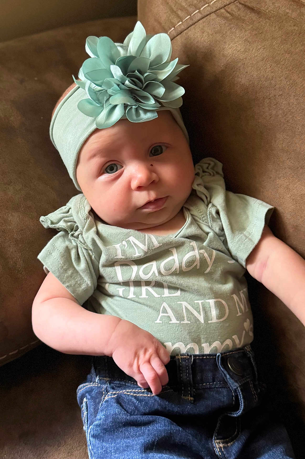 Adilynn is registered to the contest to win money with this photo: baby, casual, child, clothing, couch, cute, expression, fabric, flower, green_shirt, headband, indoor, infant, jeans, portrait, relaxed, sitting, skin, small_hand, soft_light