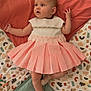 baby, infant, child, dress, pink_dress, socks, blanket, patterned_blanket, lying_down, curious_expression, soft_lighting, indoors, cute, young_child, portrait, face, hands, legs, colorful, comfortable