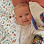 baby, smiling, infant, blanket, patterned_blanket, soft_toys, cushion, white_outfit, floral_pattern, cute, child, indoors, portrait, happy, lying_down, playtime, colorful, baby_clothes, face, head