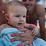 baby, towel, hand, orange_nail_polish, amber_necklace, person, smile, adult, skin, face, close_up, outdoor, poolside, blurred_background, family, affection, holding, summer, happy, portrait