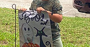 Isaiah is registered to the contest to win money with this photo: child, toddler, smiling, outdoor, halloween, costume, yard_sign, ghost, pumpkin, black_cat, spooky, grass, street, cars, parking, camouflage_shirt, shorts, sandals, portrait, daylight