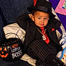 Isaiah is registered to the contest to win money with this photo: child, toddler, boy, portrait, sitting, couch, fedora, feather, suit, pinstripe, tie, red_tie, necklace, dollar_sign, shoes, pumpkin_bucket, halloween, little_boss, indoors, smiling