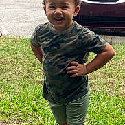 Isaiah joined the competition — help win amazing prizes! child, toddler, portrait, outdoor, grass, lawn, parked_car, vehicle, camouflage_shirt, shorts, standing, hands_on_hips, curly_hair, smiling, facial_expression, daylight, residential, front_yard, photography, person