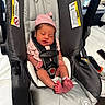 newborn, baby, car_seat, pink_hat, sleeping, infant, tiny_toes, hospital_bracelet, safety_harness, indoors, soft_lighting, cute, peaceful, child, person, baby_clothing, seat, resting, newborn_baby, closeup