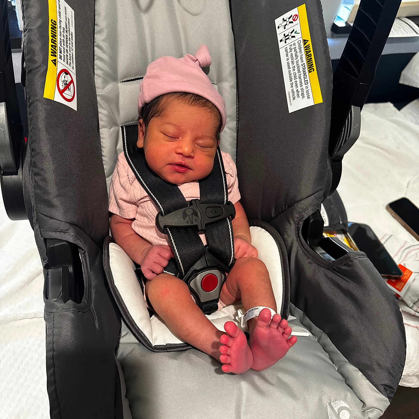 Saanvi is registered to the contest to win money with this photo: newborn, baby, car_seat, pink_hat, sleeping, infant, tiny_toes, hospital_bracelet, safety_harness, indoors, soft_lighting, cute, peaceful, child, person, baby_clothing, seat, resting, newborn_baby, closeup