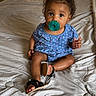 baby, child, pacifier, blue_dress, curly_hair, indoor, bed, blanket, sunlight, curtains, footwear, sitting, looking, young_child, cute, infant, person, soft_light, home, casual