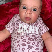 Amalie is registered to the contest to win money with this photo: baby, infant, child, onesie, clothing, leopard_print, pink, red_blanket, wide_eyes, face, skin, cute, expression, lying_down, plush, soft_texture, human, portrait, indoors, newborn