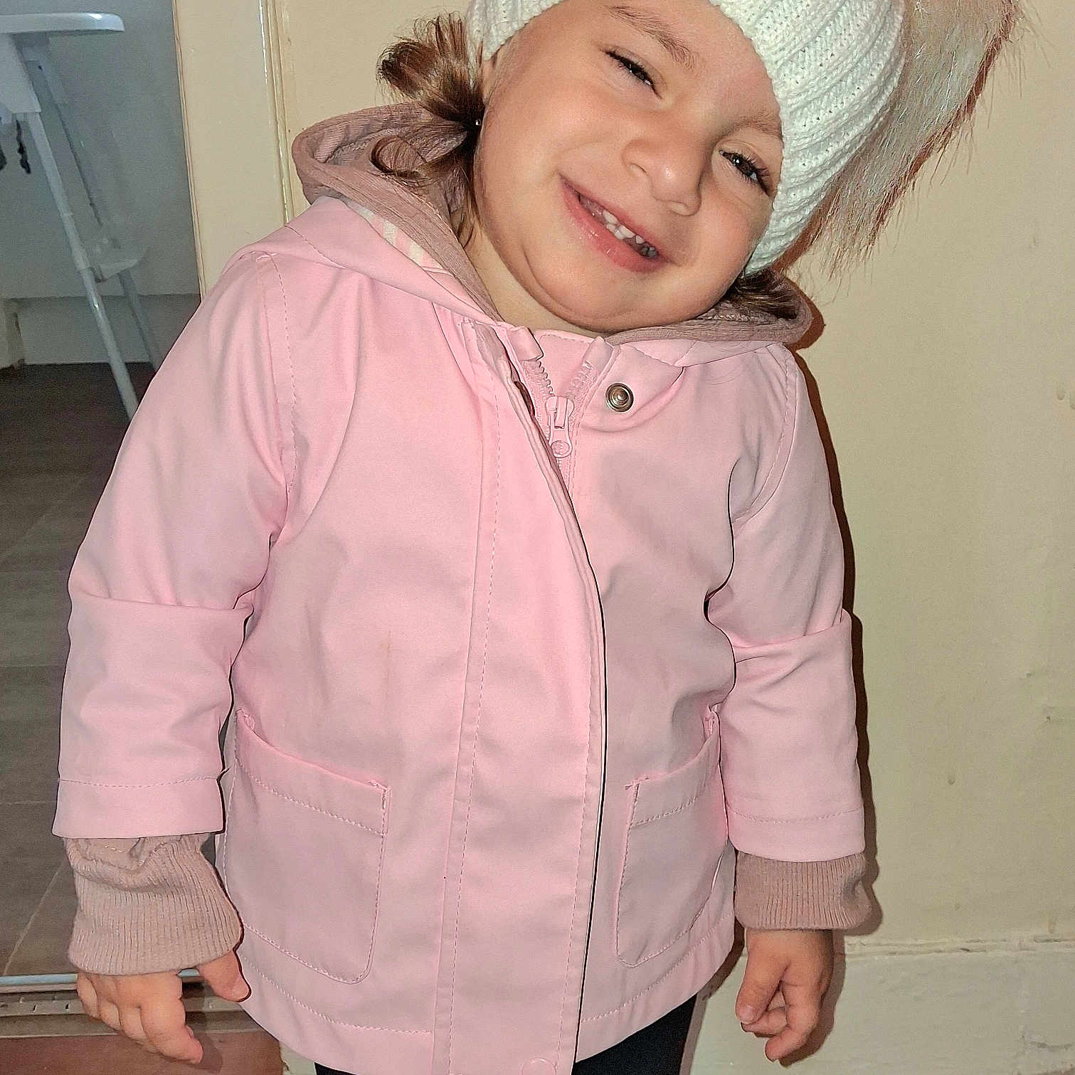 Amalie joined the competition — help win amazing prizes! child, clothing, cute, door, face, floor, happy, hat, head_tilt, indoor, knit_hat, long_sleeve, person, pink_jacket, pom_poms, portrait, smile, standing, warm_clothing, young