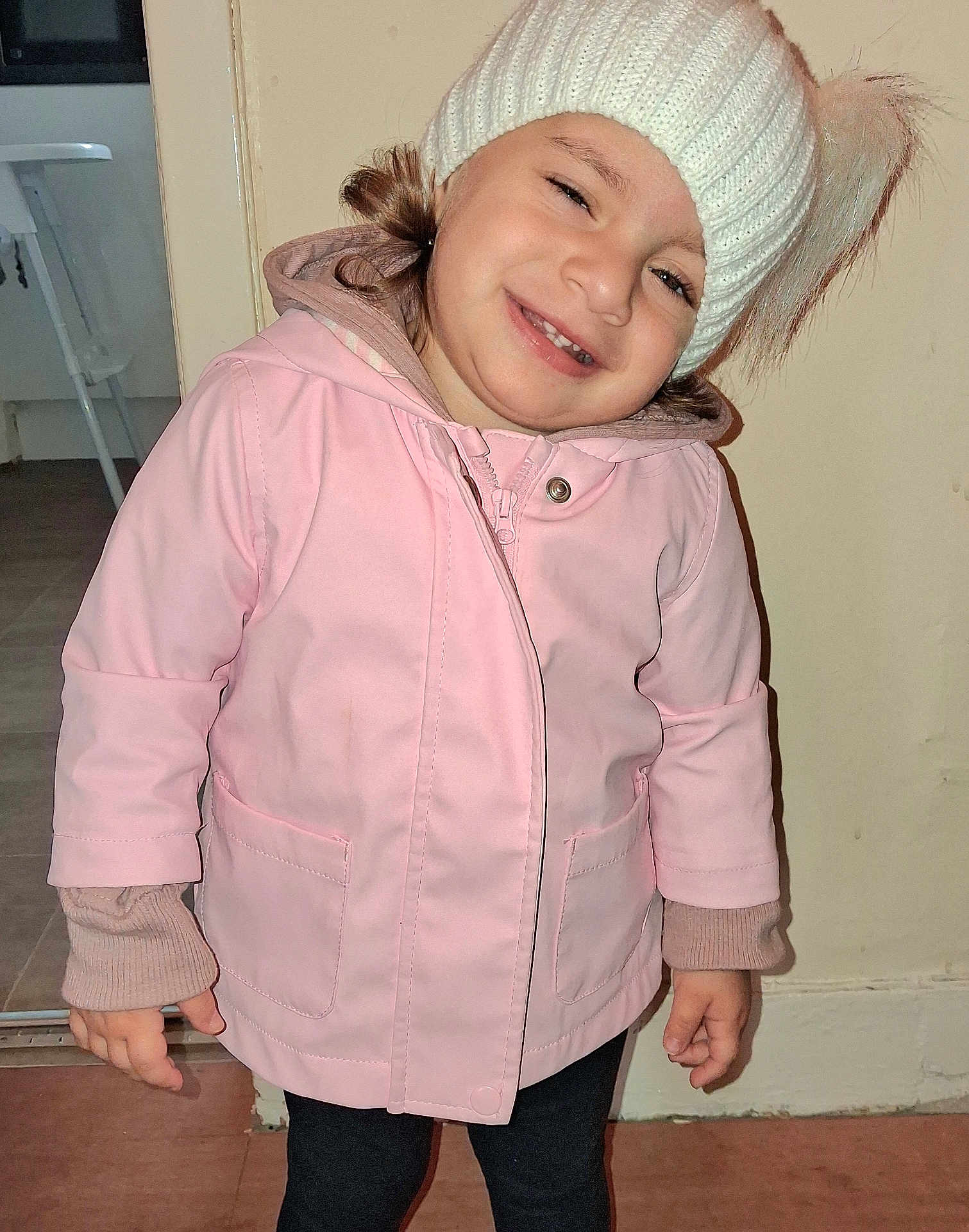 Amalie joined the competition — help win amazing prizes! child, smile, hat, knit_hat, pom_poms, pink_jacket, indoor, person, face, happy, portrait, clothing, long_sleeve, standing, floor, door, head_tilt, cute, warm_clothing, young