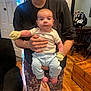 Emilio joined the competition — help win amazing prizes! baby, person, indoor, clothing, mittens, pants, floor, wooden_floor, furniture, chair, table, window, door, car_seat, tattoo, hand, face, expression, holding, home