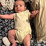 Emilio is registered to the contest to win money with this photo: baby, infant, onesie, blanket, pillow, soft_toy, elephant_toy, floral_pattern, lying_down, cute, indoors, child, skin, face, arm, leg, foot, sleeping_area, cozy, newborn