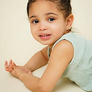 Elif is registered to the contest to win money with this photo: child, toddler, portrait, smile, eyes, braids, earring, sleeveless_top, soft_skin, closeup, studio_shot, neutral_background, lying_down, forearm, hands, warm_tone, innocence, candid, texture, gaze