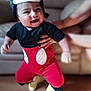 baby, child, smiling, costume, mickey_mouse, hat, red_pants, yellow_shoes, indoor, living_room, couch, wooden_floor, person, cute, happy, playful, infant, hand, holding, blurred_background