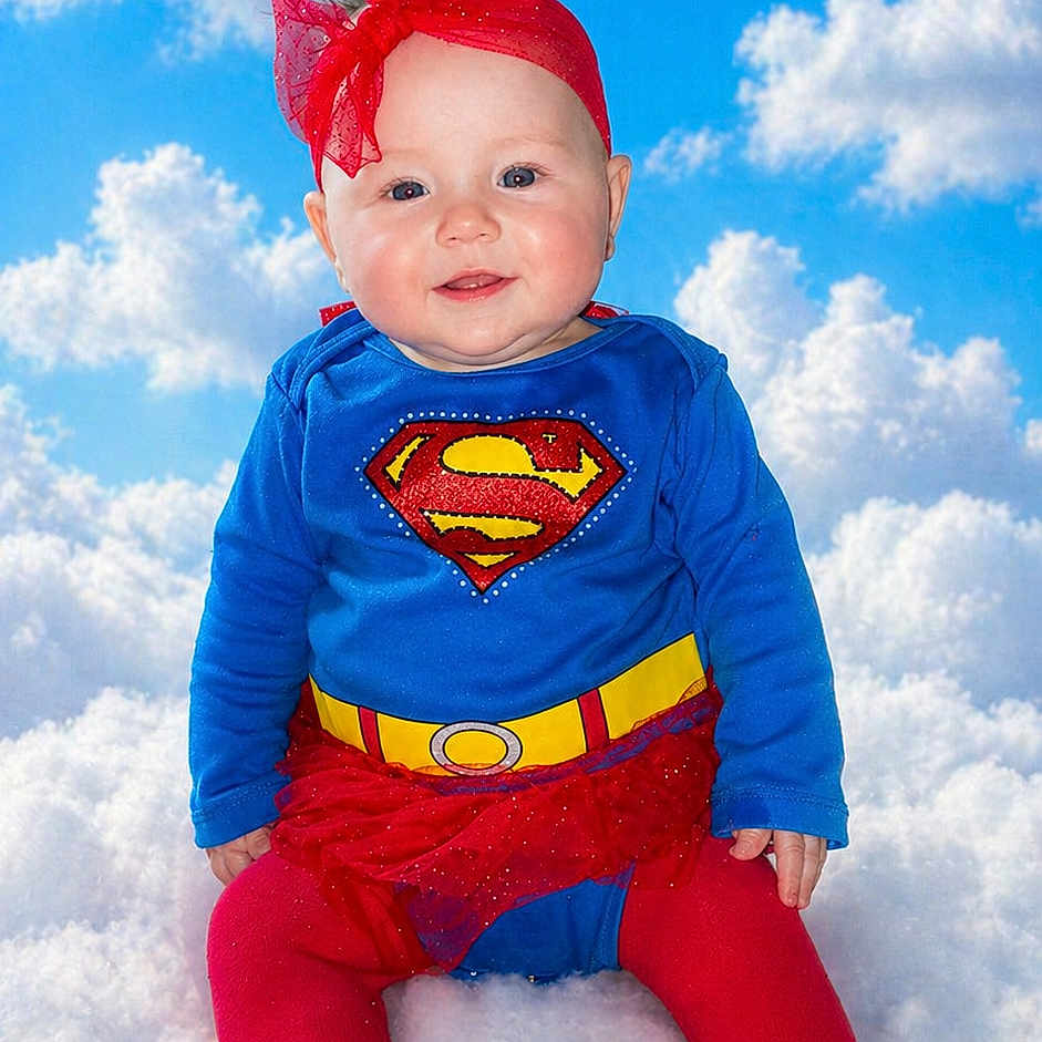 Zhelda joined the competition — help win amazing prizes! baby, child, superhero_costume, blue_sky, clouds, red_headband, red_tights, red_skirt, smiling, cute, portrait, infant, outdoor_style_background, fluffy_surface, colorful_clothing, happy, costume, playful, sitting, bright