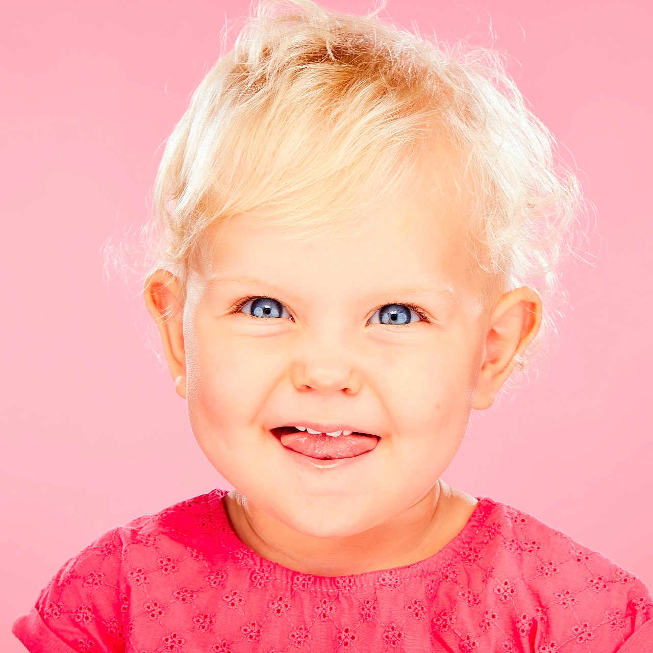 Jeanne a rejoint le concours — aidez-le/la à gagner de superbes lots ! baby, blond_hair, blue_eyes, child, close_up, cute, expression, face, fashion, happy, innocent, pink_background, pink_dress, playful, portrait, smiling, studio_photo, toddler, tongue_out, young_child