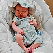 Silas joined the competition — help win amazing prizes! baby, baby_seat, child, clothing, comfortable, cushion, cute, expression, hat, headwear, indoor, infant, light_blue, newborn, overalls, person, portrait, resting, small_feet, wood_floor