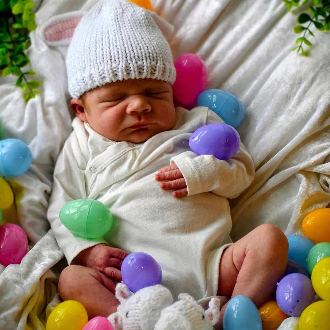 Silas is registered to the contest to win money with this photo: newborn, baby, sleeping, white_hat, knitted, easter_eggs, colorful, basket, blanket, booties, soft, cute, infant, resting, indoors, peaceful, small, cozy, hand, wrapped