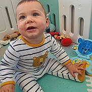 Lyam a rejoint le concours — aidez-le/la à gagner de superbes lots ! baby, child, pajamas, striped_clothing, toy, playmat, indoor, smiling, face, hand, sitting, floor, cute, expression, head, person, infant, plush_toy, colorful, playpen