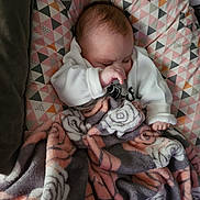 Bryan participe au concours pour gagner de l'argent avec cette photo : baby, infant, newborn, sleeping, blanket, floral_blanket, geometric_pattern, bedding, cozy, white_clothing, face, hand, forehead, cheek, hair, indoor, portrait, resting, peaceful, soft_texture