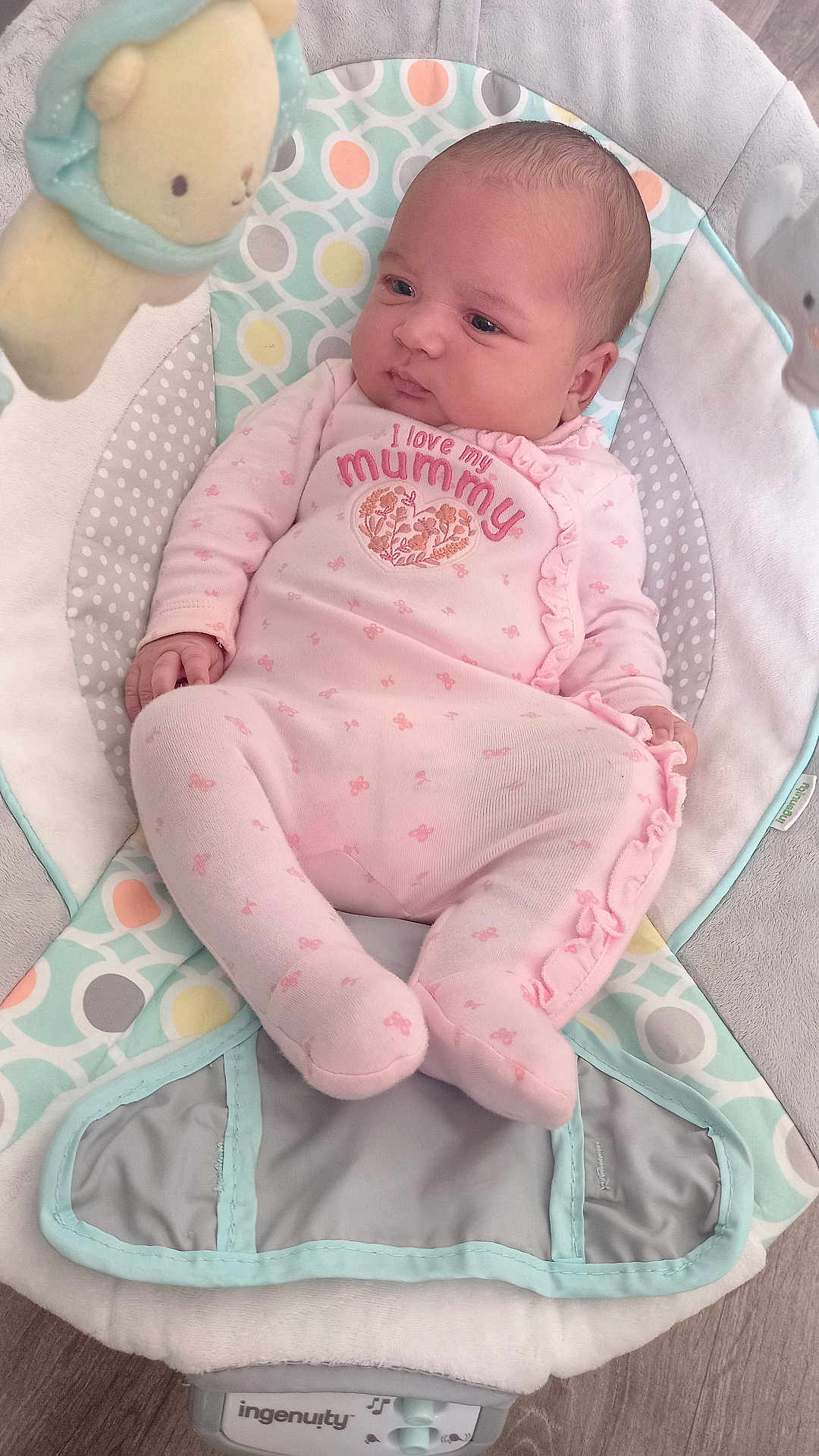 Ruby is registered to the contest to win money with this photo: baby, infant, onesie, pink_clothing, baby_rocker, plush_toy, soft_toy, flooring, patterned_fabric, child, cute, sleepwear, comfort, indoor, newborn, infant_fashion, seated, portrait, baby_girl, relaxed