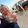 toddler, child, smiling, person, adult_hand, pony, animal, truck, dirt_ground, sunset, outdoor, clothing, jeans, patterned_shirt, sky, clouds, happy, holding, fence, rural